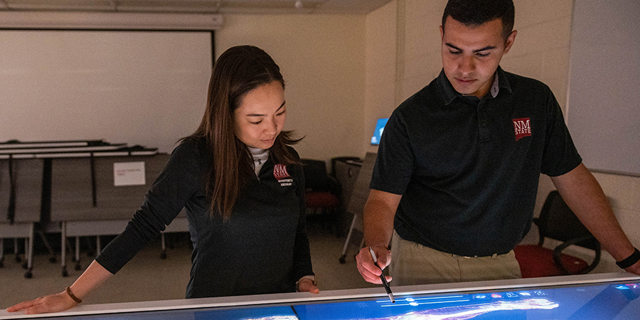 A male and female student work on an anatomically correct digital rendering of the muscles in a human body. 