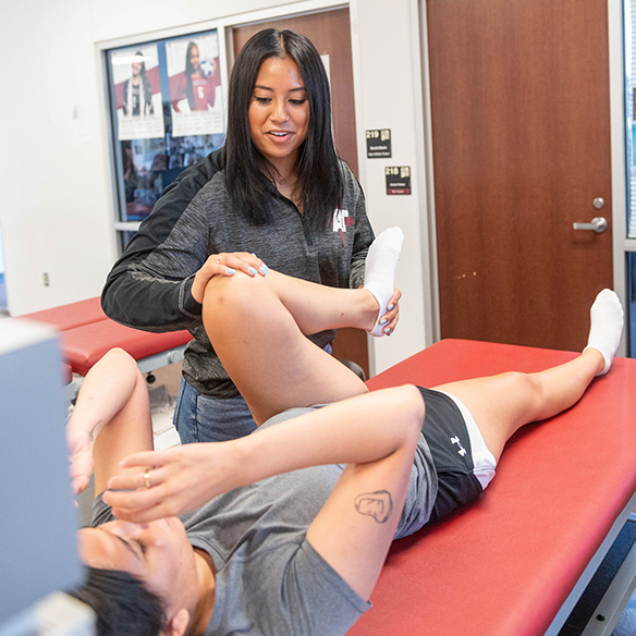 An athletic training student helps an athlete stretch her leg