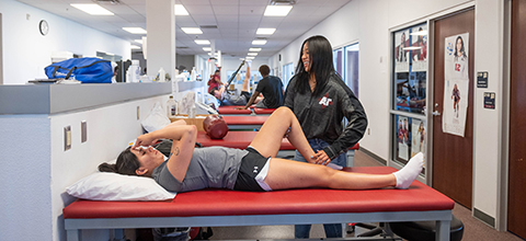 An athletic trainer helps an athlete stretch out her leg while laying on a table. 