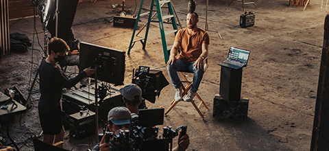 A film crew surrounding a man sitting on a stool.