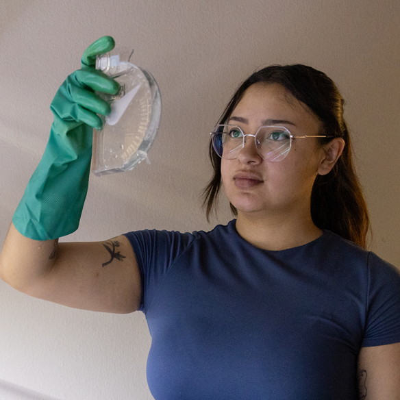 Hispanic female student looking at a water sample in a biology lab on a college campus.