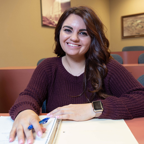 a female student smiling with a notebook and pen in front of her at a table