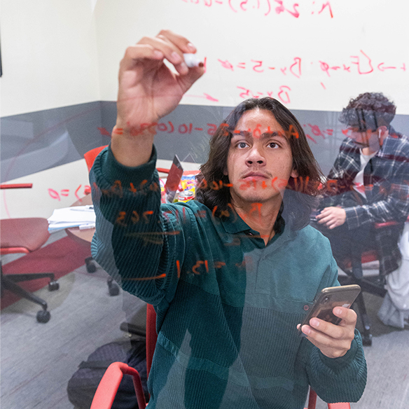 student writing equations on a glass wall