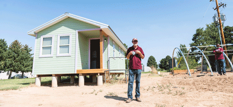 Man in front of tiny home on farmland.