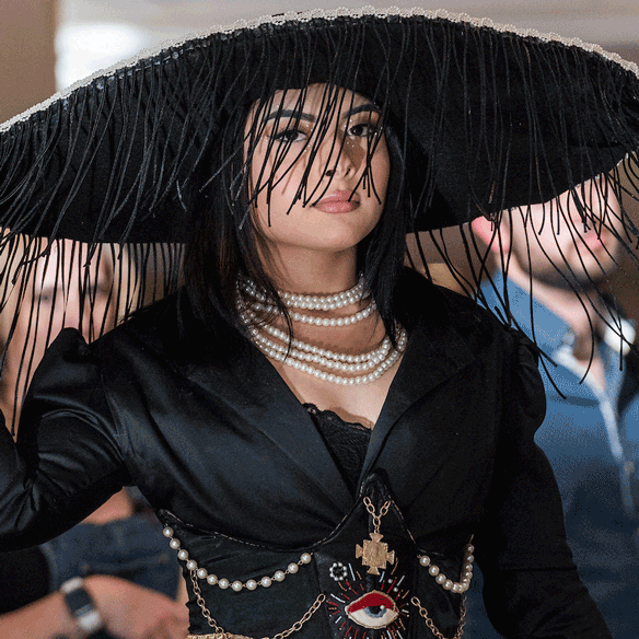 Student in black dress and large black hat modeling at a fashion show.