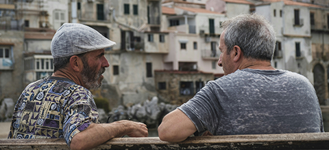 Two men sitting beside each other talking.
