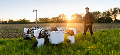 Male mechanical engineer with sustainable agricultural robot in field