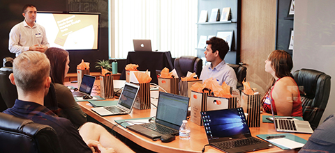 A team of business employees sitting at a conference table with laptops listening to a speaker